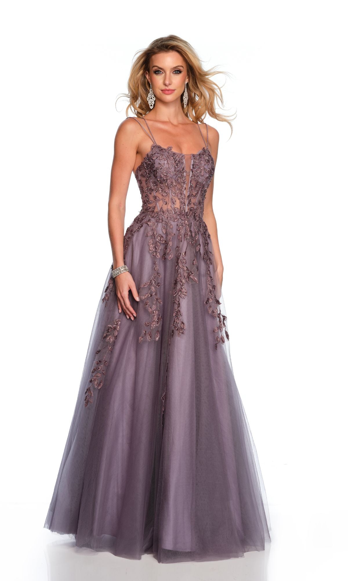 A woman wearing the Long Formal Dress 11653 by Dave and Johnny—a lavender A-line tulle ball gown with floral appliqué, lace embroidery, thin straps, and a sheer bodice—stands against a white background.